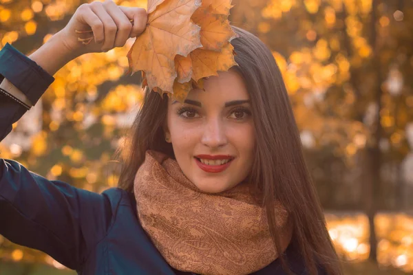 Retrato de hermosas chicas sonrientes con el pelo liso y una bufanda caliente que levantó las hojas de su mano de cerca —  Fotos de Stock