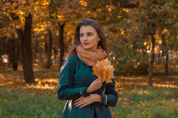 Giovane ragazza si trova sulla strada vicino agli alberi distoglie lo sguardo e tiene le foglie in mano — Foto Stock