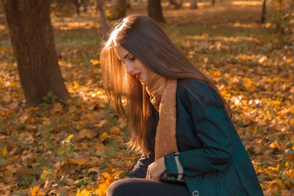 Jeune fille aux longs cheveux raides s'assoit dans le parc, tournant latéralement — Photo