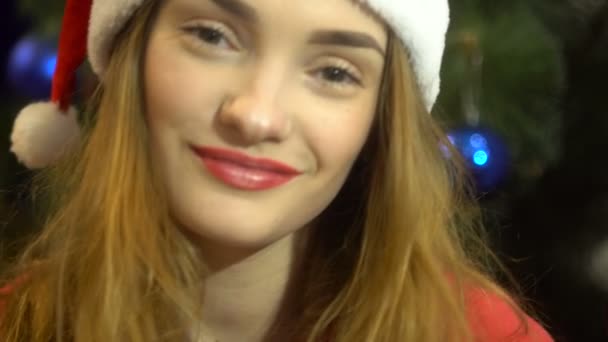 Красива молода дівчина в капелюсі Санта дивиться на камеру і посміхається — стокове відео