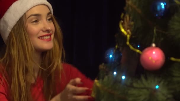 Schönheit junge Frau mit Weihnachtsmütze lächelt und tänzelt einen Weihnachtsbaum — Stockvideo