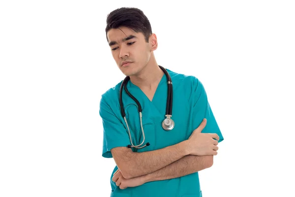 Pensativo jovem médico masculino com estetoscópio em uniforme posando isolado no fundo branco — Fotografia de Stock