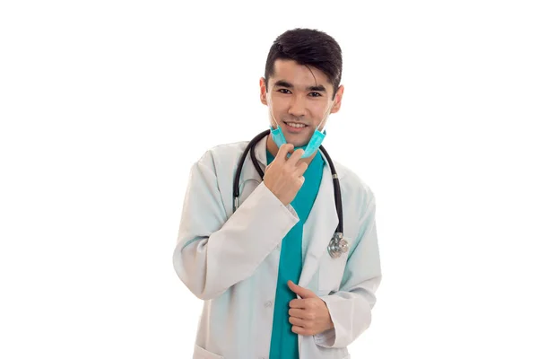 Joven médico masculino con estetoscopio en uniforme y máscara posando aislado sobre fondo blanco — Foto de Stock