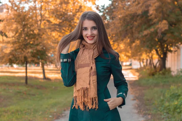 Молодая девушка в длинном шарфе улыбается, стоя в парке — стоковое фото