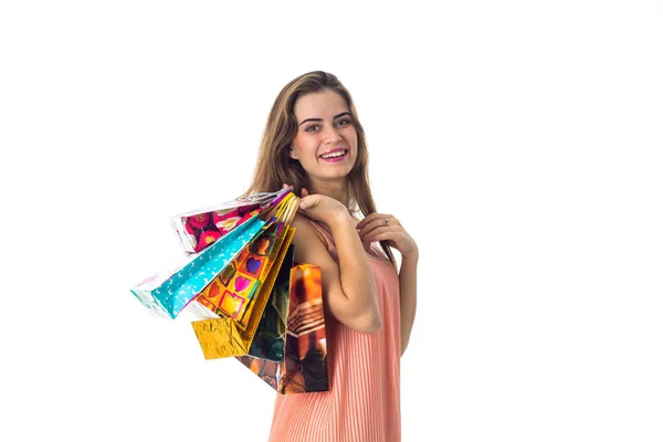Улыбающаяся молодая девушка держит на плече много ярких подарочных пакетов, изолированный белый фон — стоковое фото
