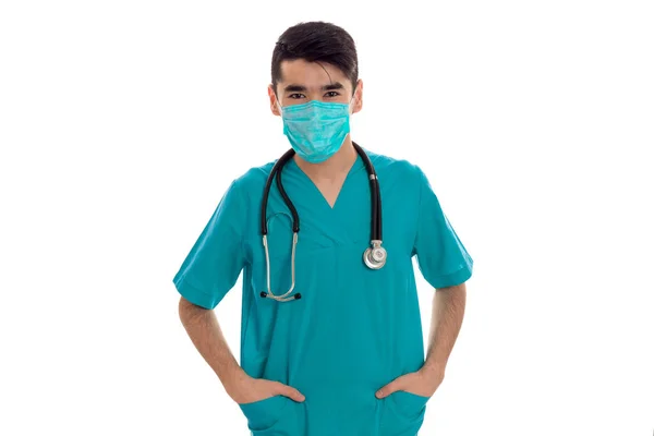 Joven doctor masculino en uniforme y máscara con estatoscopio posando aislado sobre fondo blanco — Foto de Stock