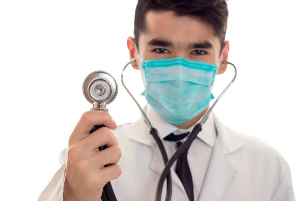 Primer plano del joven médico en uniforme y máscara con el stathoscope posando aislado sobre fondo blanco —  Fotos de Stock