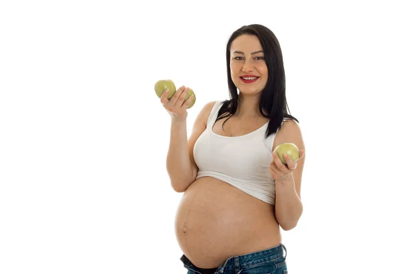 Cheerful pregnant brunette woman with big belly posing with green apples in hands isolated on white background — Stock Photo, Image