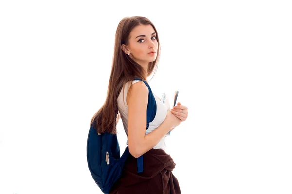 Втомлена молода студентка дівчина з блакитним рюкзаком на плечі і папках для блокнотів в руках дивиться на камеру ізольовано на білому тлі — стокове фото