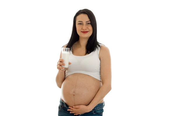 Ganska ung gravid brunett kvinna röra hennes mage och drycker mjölk isolerad på vit bakgrund — Stockfoto