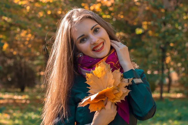 Retrato de uma jovem menina sorridente com cabelos longos e lisos que mantém as folhas secas na mão — Fotografia de Stock