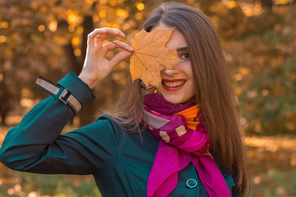 Улыбающаяся молодая девушка с кленовым листом рядом с глазом крупным планом — стоковое фото