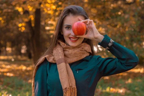 Jovem menina em cachecol longo mantém a Apple perto dos olhos e sorrisos — Fotografia de Stock