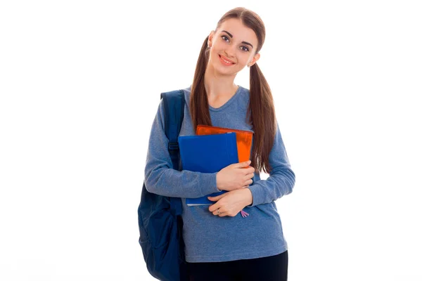 Wesoły, młody student brunetka dziewczyna z niebieskim backpackand wiele książek w jej ręce, pozowanie i patrząc na kamery i uśmiecha się na białym tle na białym tle — Zdjęcie stockowe