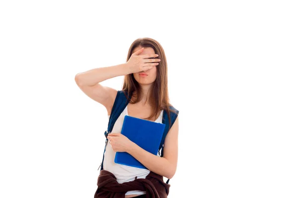 Giovane ragazza studentessa bruna con zaino blu e un sacco di libri nelle sue mani in posa e guardando la fotocamera isolata su sfondo bianco — Foto Stock