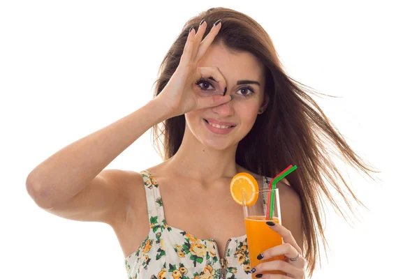 Γοητευτική νεαρή μελαχρινή κοπέλα στο καλοκαίρι ρούχα με λουλουδάτο μοτίβο shoing Ok και ποτά πορτοκάλι κοκτέιλ απομονώνονται σε λευκό φόντο — Φωτογραφία Αρχείου