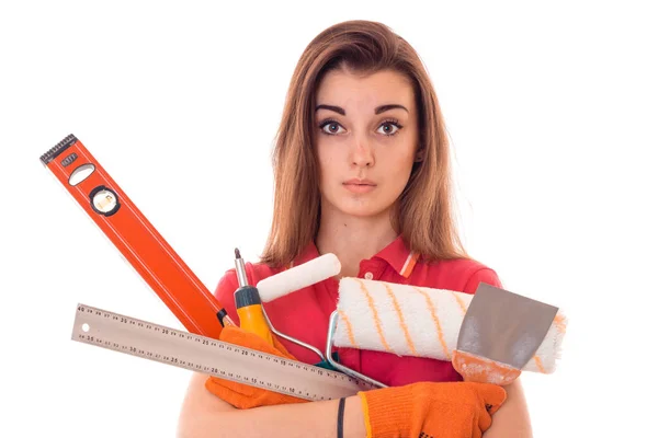 Sorprendida joven constructora morena en uniforme hace renovación con herramientas en sus manos aisladas sobre fondo blanco — Foto de Stock
