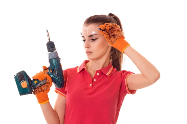 Cutie joven chica constructora morena en uniforme y gafas hace renovación con taladro en las manos aisladas sobre fondo blanco — Foto de Stock