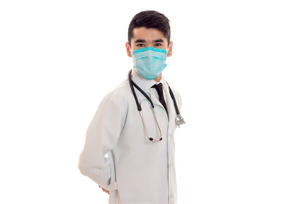 Giovane elegante medico bruna in uniforme e maschera con stetoscopio isolato su sfondo bianco — Foto Stock