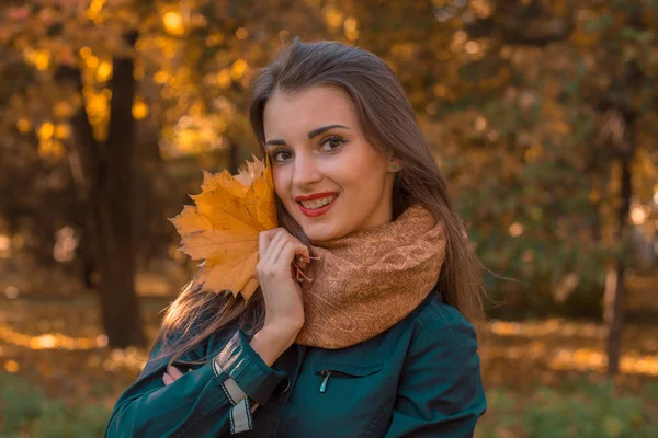 Красивая девушка с красными губами стоит на улице и держит возле лица сухие листья — стоковое фото