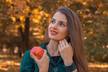 Kırmızı dudaklar gülümseyen kızla uzaktan bakar ve elma elinde tutar