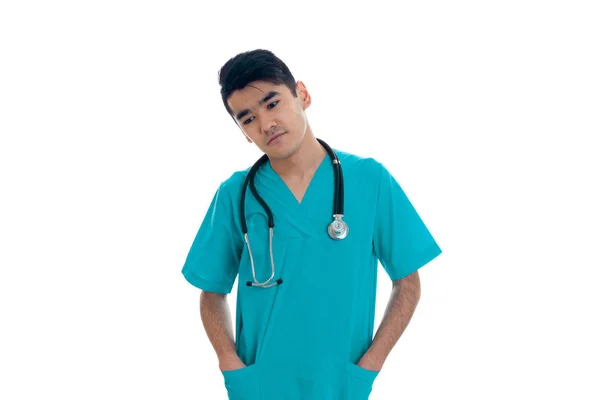 Elegante jovem morena homem médico em azul uniforme posando isolado no fundo branco — Fotografia de Stock