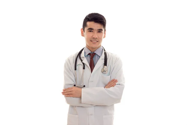 Grazioso giovane bruna uomo medico in uniforme bianca con stetoscopio guardando e sorridendo sulla macchina fotografica isolata in studio — Foto Stock