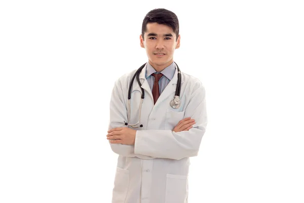 Beau jeune homme brunette médecin en uniforme blanc avec stéthoscope regardant et souriant sur la caméra isolé en studio — Photo