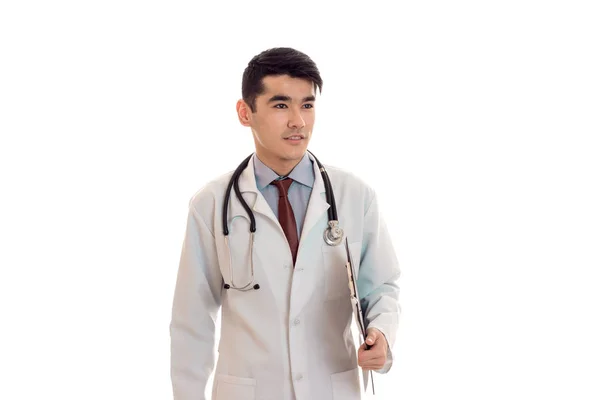 Guapo joven morena hombre médico en uniforme blanco con estetoscopio mirando a un lado aislado en estudio — Foto de Stock