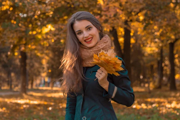 Молодая девушка улыбается и держит в руке листья с деревьев — стоковое фото