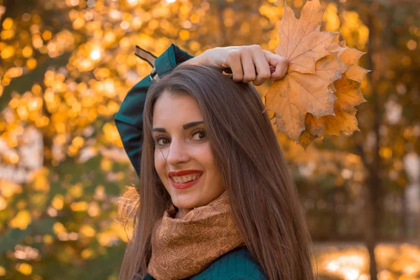 Retrato de una hermosa chica encantadora que mantiene las hojas por encima de su cabeza y sonríe ante el plan krupnyy — Foto de Stock