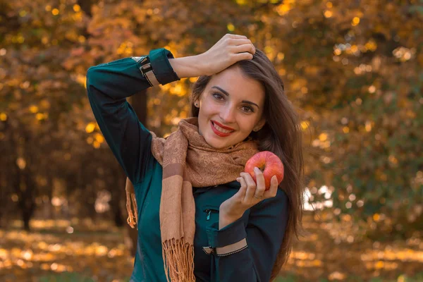 Χαρούμενο κορίτσι στέκεται σε το πάρκο κρατά τα μαλλιά με το ένα χέρι ενώ ο άλλος κατέχει Apple — Φωτογραφία Αρχείου