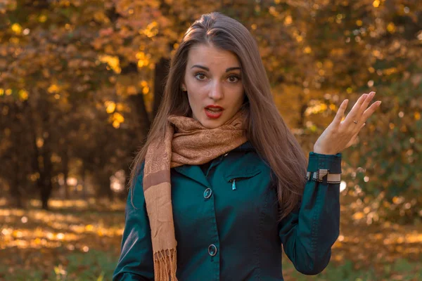 Zabawna dziewczyna stoi w parku otwierając usta i rozprzestrzenia się jej rękę — Zdjęcie stockowe