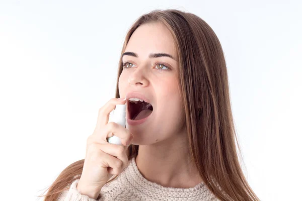 Молодая девушка, брызгающая спреем для горла изолирован на белом фоне — стоковое фото