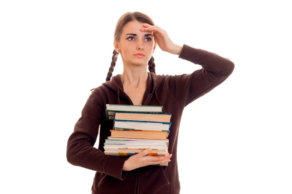 Уставшая умная студентка в коричневой спортивной одежде с большим количеством книг в руках позирует изолированно на белом фоне — стоковое фото