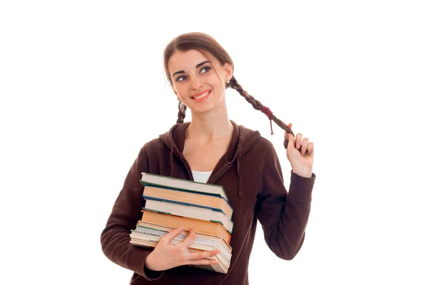 白色背景上孤立的开朗聪明的学生女孩在棕色运动衣服用了很多书在她一只手触摸她的头发和微笑 — 图库照片