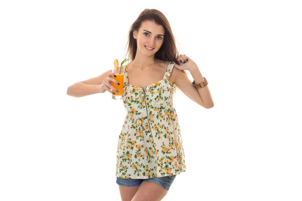 아름다움 꽃 패턴으로 빛 sarafan에서 갈색 머리 여자 카메라 흰색 배경에 고립 된 오렌지 칵테일 및 미소 음료 — 스톡 사진