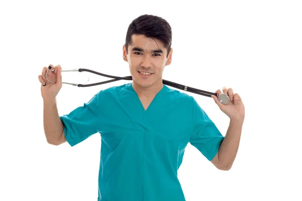 Ritratto di giovane bel bruna uomo medico in uniforme blu con stetoscopio guardando e sorridendo sulla macchina fotografica isolata su sfondo bianco — Foto Stock