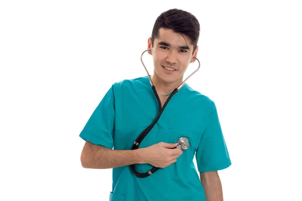 Retrato de jovem morena bonita homem médico em uniforme azul com estetoscópio olhando e sorrindo na câmera isolada no fundo branco — Fotografia de Stock