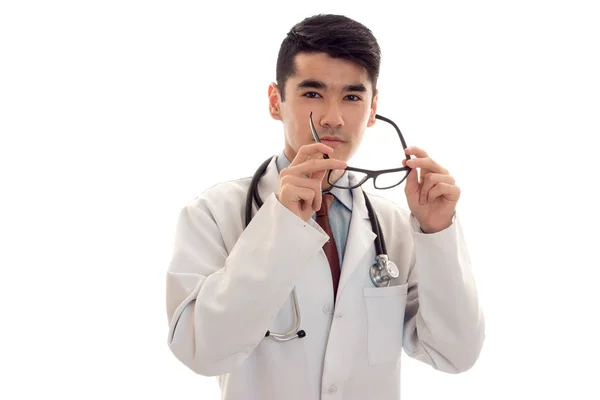 Ritratto di giovane bello bruna uomo medico in uniforme bianca togliersi gli occhiali e posa sulla macchina fotografica isolato su sfondo vuoto — Foto Stock