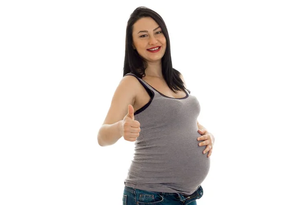 Porträtt av ung vacker gravid kvinna röra hennes mage och visar tummen isolerade på vit bakgrund — Stockfoto