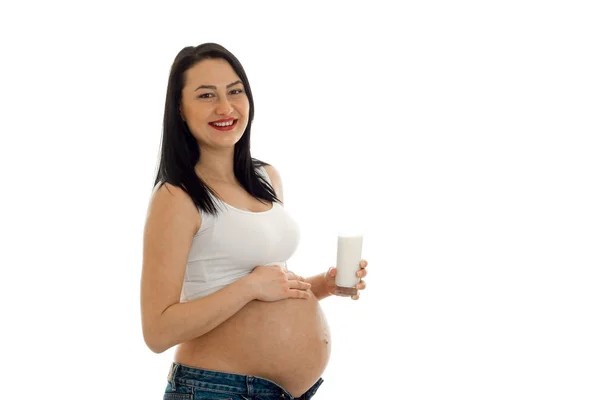 Portrait of young funny pregnant woman with glass of milk touching her belly and smiling on camera isolated on white background — Stock Photo, Image