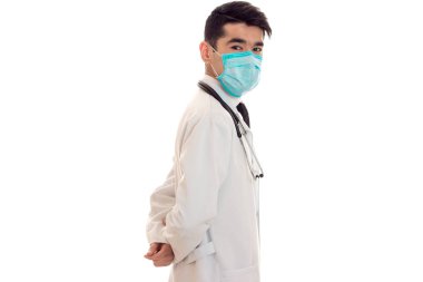 Beyaz önlük doktor yan yüzünde beyaz arka plan üzerinde izole bir maske ile duruyor.