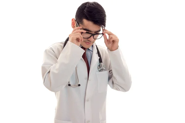 Un giovane medico in camice bianco che tiene su le mani per gli occhiali isolati su sfondo bianco — Foto Stock