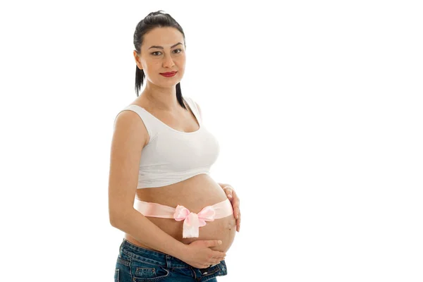 Μια νεαρή έγκυο γυναίκα στέκεται προς τα πλάγια με μια κορδέλα για το στομάχι που απομονώνονται σε λευκό φόντο — Φωτογραφία Αρχείου
