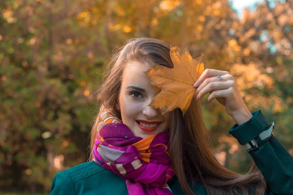 Menina em um lenço ao redor do pescoço mantém as folhas secas perto do olho close-up — Fotografia de Stock