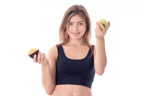 Deportiva chica de pie recta y sosteniendo un cupcake manzana aislado sobre fondo blanco — Foto de Stock