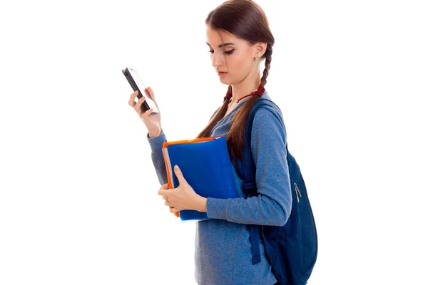 Junge intelligente brünette Studentin mit Rucksack auf den Schultern liest ein Buch und telefoniert isoliert auf weißem Hintergrund — Stockfoto