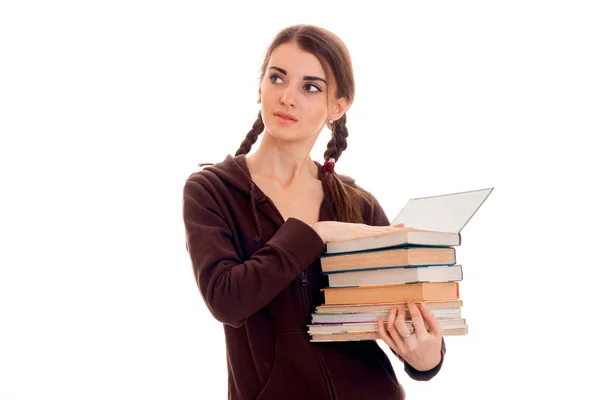 Junge hübsche brünette Studentin in brauner Sportkleidung mit Zöpfen und Büchern in den Händen, die isoliert auf weißem Hintergrund wegschauen — Stockfoto