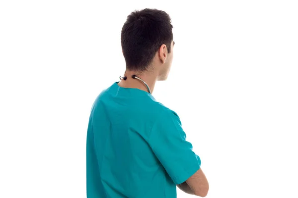 Young brunette man doctor in blue uniform with stethoscope on his shoulders looking away from behind isolated on white background — Stock Photo, Image